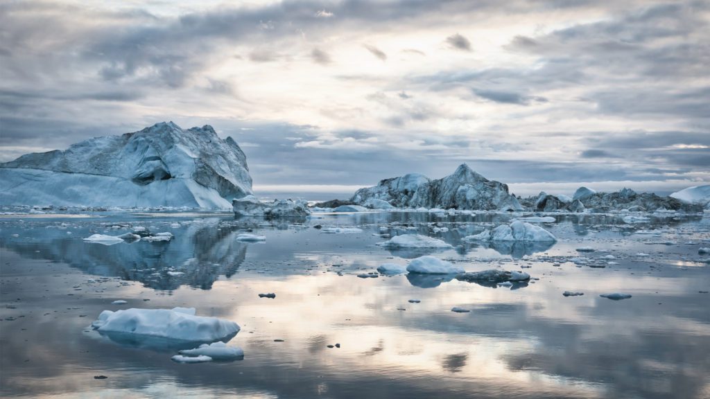 Large arctic Iceberg drifting on the polar waters under moody sunset skyscape, cloudscape mirroring in the calm water